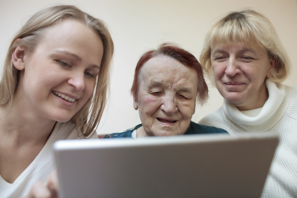 Three women of different ages smiling using a smart tablet