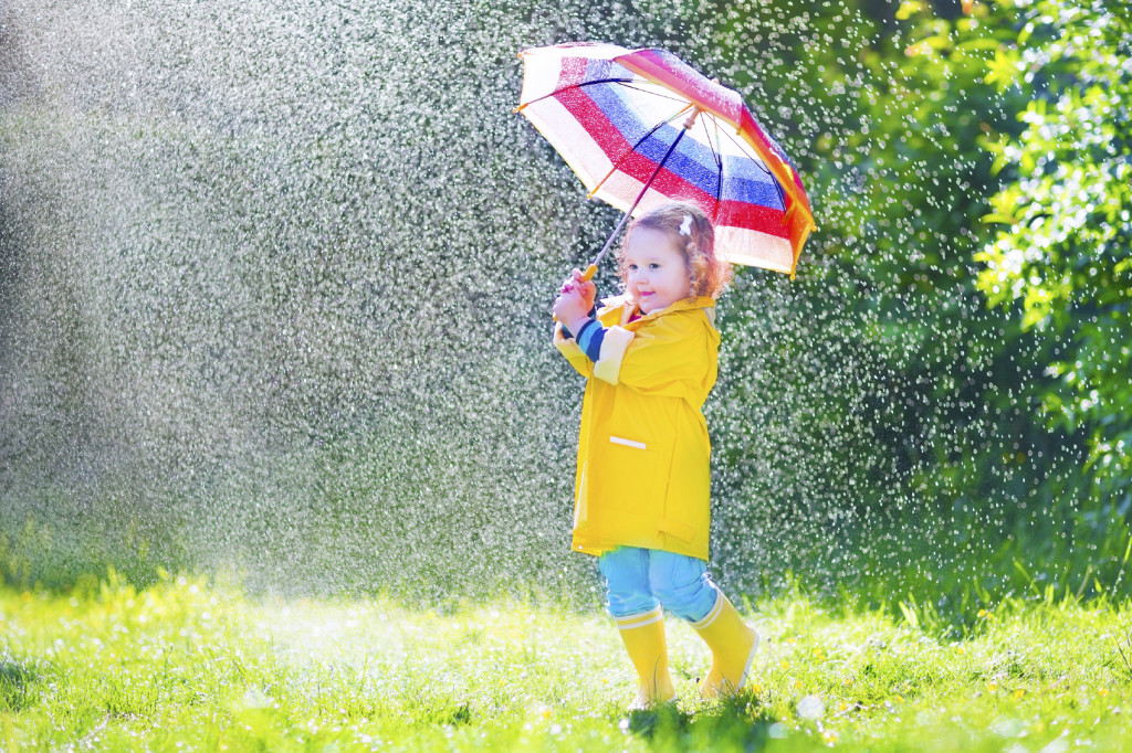 Funny toddler with umbrella playing in the rain