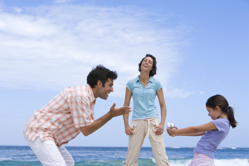 Family of three on beach, daughter with camcorder